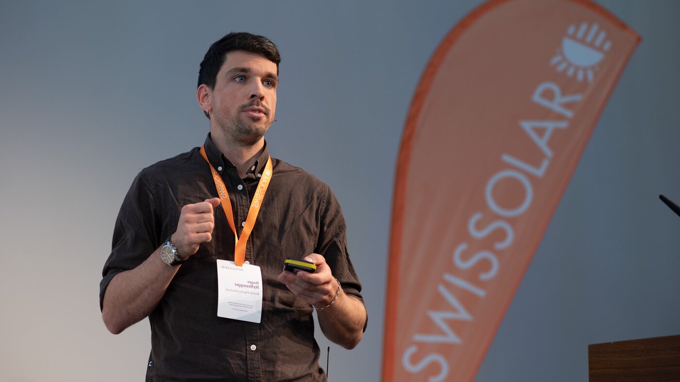 Mann mit orangener Flagge im Hintergrund | © Swissolar / Céline Farias