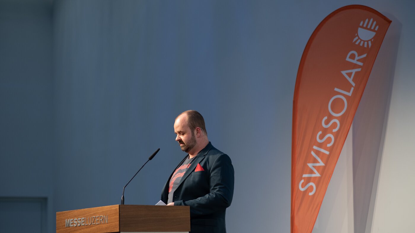Mann mit einer orangenen Flagge im Hintergrund | © Swissolar / Céline Farias