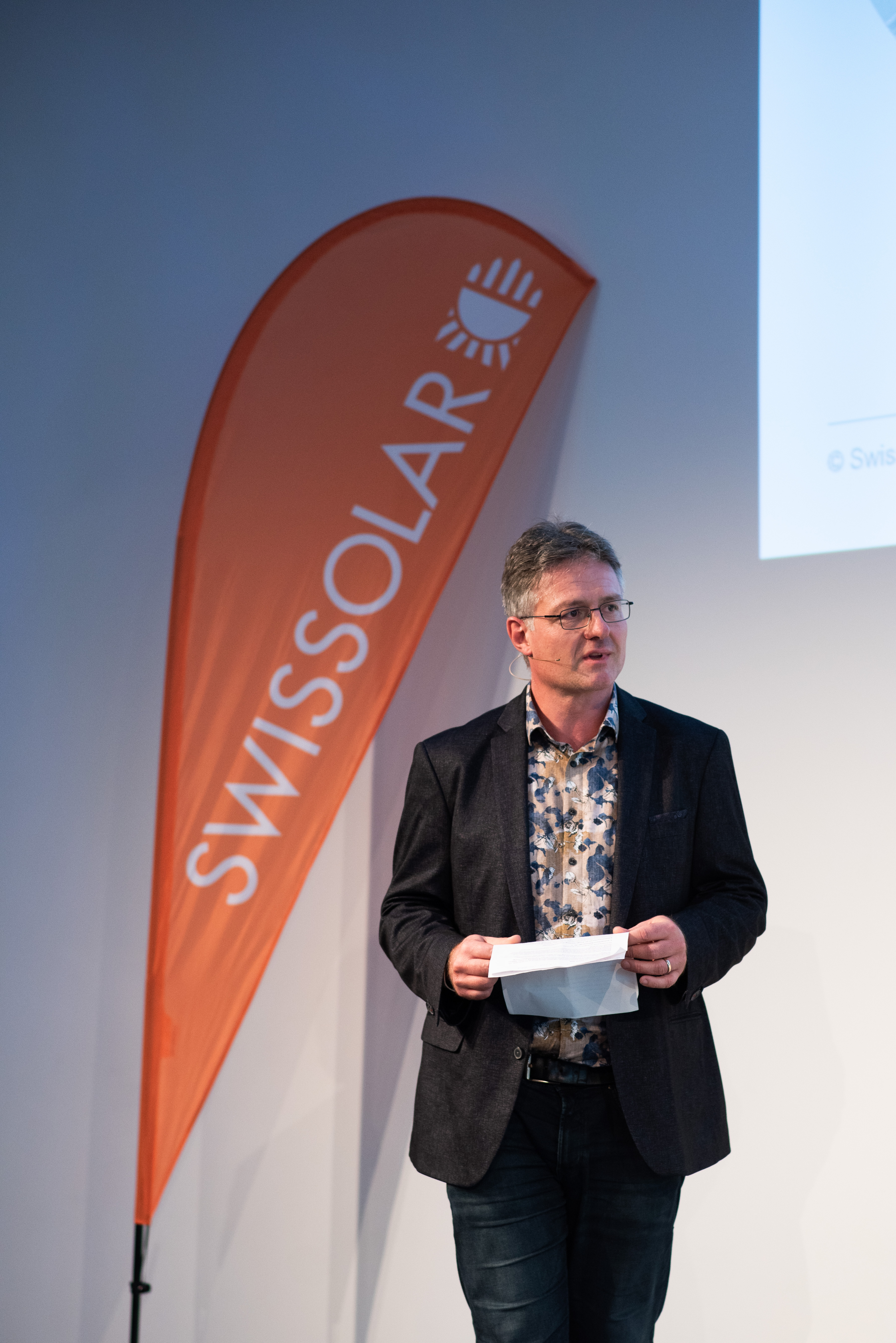 Mann mit einer orangenen Flagge im Hintergrund | © Swissolar / Céline Farias