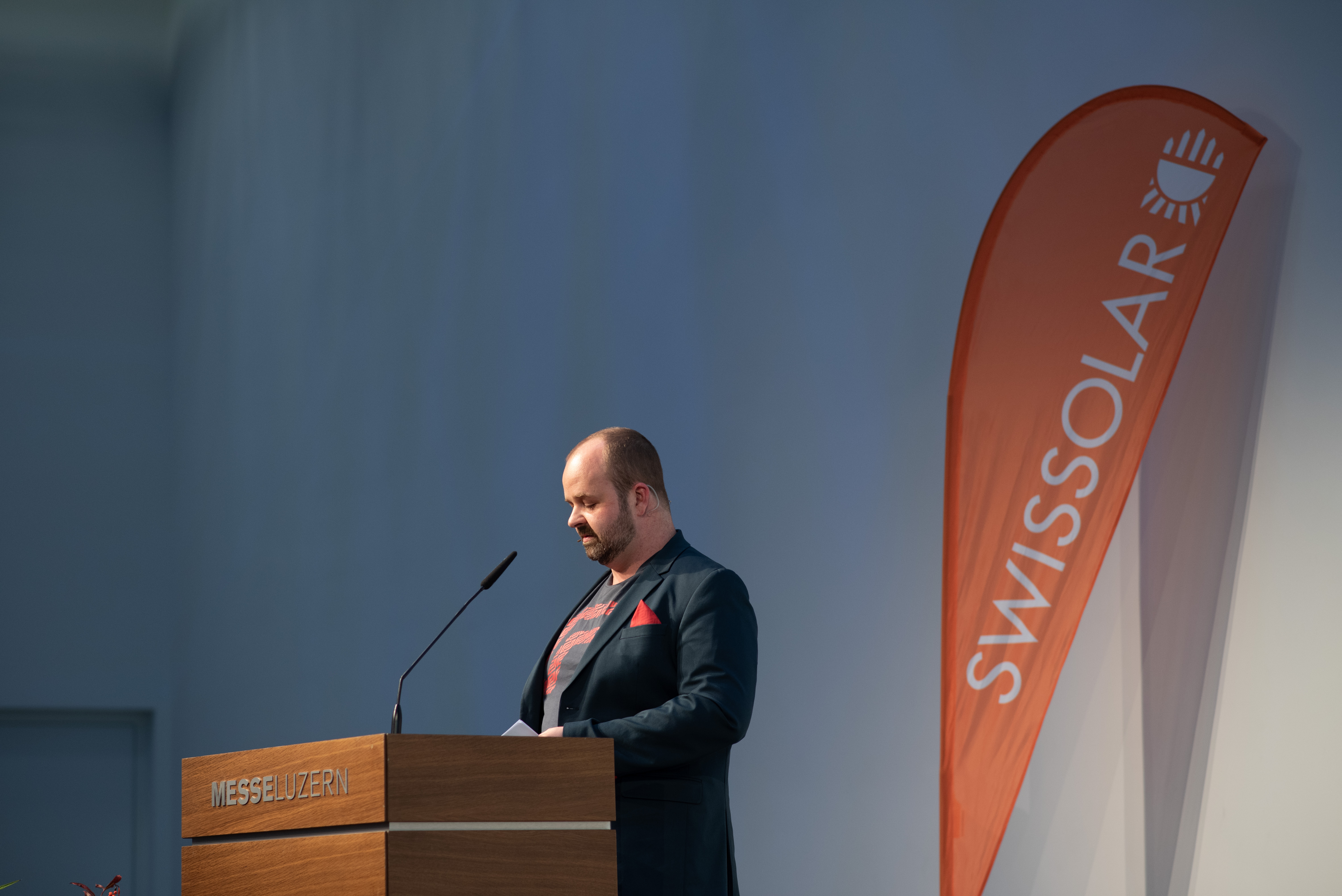 Mann mit einer orangenen Flagge im Hintergrund | © Swissolar / Céline Farias